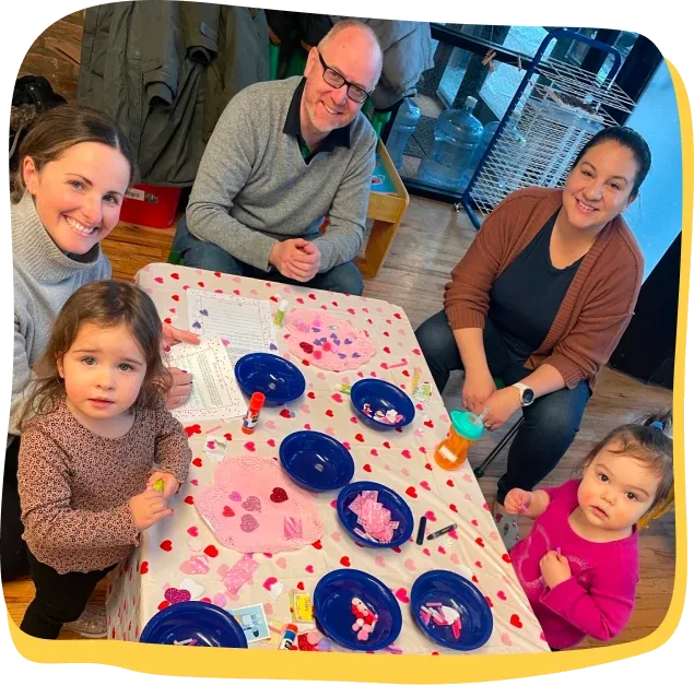Parents join their toddlers for a Valentine’s celebration craft table in a Songbird Academy classroom