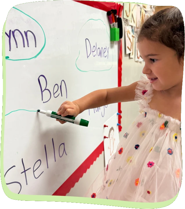 A preschooler writes classmates names on the whiteboard at Songbird Academy