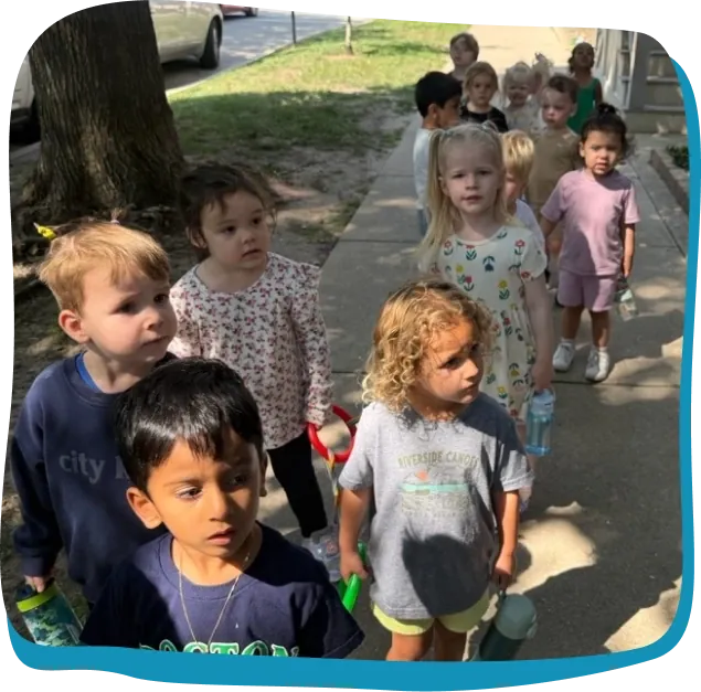 A line of Songbird Academy preschoolers walks along the sidewalk on a neighborhood outing