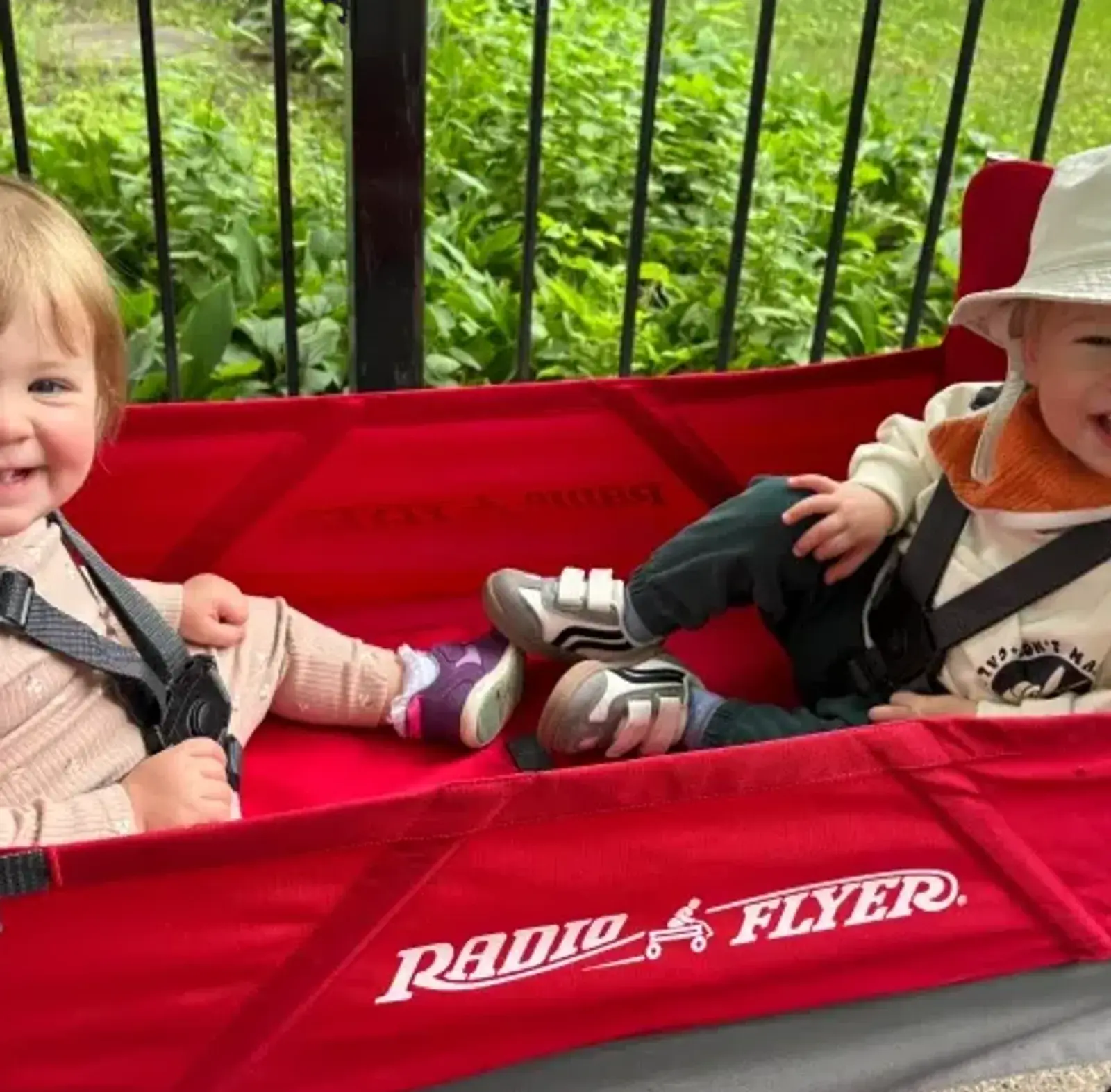 Two smiling toddlers riding in a red wagon outdoors on a Songbird Academy neighborhood walk in Chicago