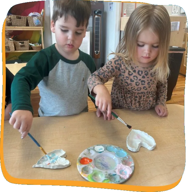 Two toddlers painting clay hearts together at a Songbird Academy classroom table