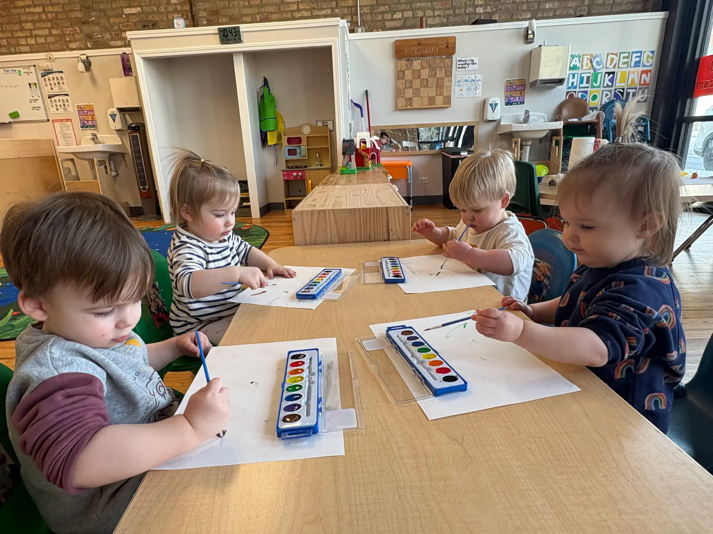 Four toddlers painting with watercolors at a shared table in a Songbird Academy classroom in Chicago